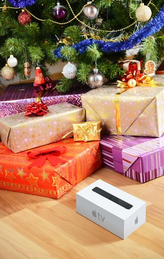 Rendering of Apple TV set-top device packaging undwrapped under Christmas Tree